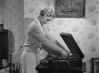 Movie still from “Monsieur Hulot's Holiday” (1953), directed by Jacques Tati – An old photo of a woman using a record player; Medium shot, High angle