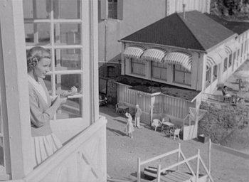 Movie still from “Monsieur Hulot's Holiday” (1953), directed by Jacques Tati – An old black and white photo of a woman looking out of a window; Wide shot, Low angle