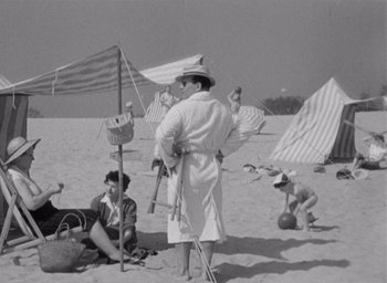 Movie still from “Monsieur Hulot's Holiday” (1953), directed by Jacques Tati – A group of people sitting on top of a sandy beach; Wide shot, High angle