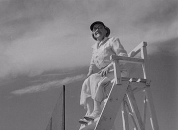 Movie still from “Monsieur Hulot's Holiday” (1953), directed by Jacques Tati – An older woman sitting on a lifeguard chair; Medium shot, Low angle