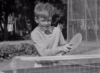 Movie still from “Monsieur Hulot's Holiday” (1953), directed by Jacques Tati – A young boy holding a tennis racquet on top of a tennis court; Medium shot, High angle