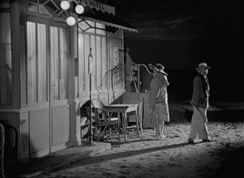 Movie still from “Monsieur Hulot's Holiday” (1953), directed by Jacques Tati – Two men walking on the beach at night near a hotel; Wide shot, Over the shoulder angle