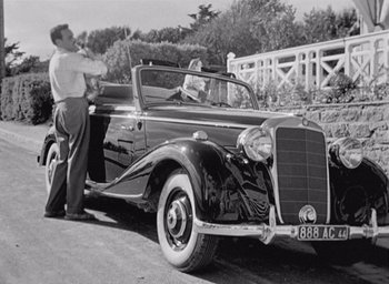 Movie still from “Monsieur Hulot's Holiday” (1953), directed by Jacques Tati – An old photo of two men in a car; Wide shot, High angle