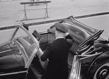 Movie still from “Monsieur Hulot's Holiday” (1953), directed by Jacques Tati – An old photo of a man loading luggage in the back of a car; Wide shot, High angle