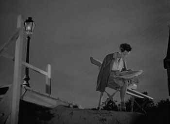 Movie still from “Monsieur Hulot's Holiday” (1953), directed by Jacques Tati – A woman standing next to a street light; Wide shot, High angle