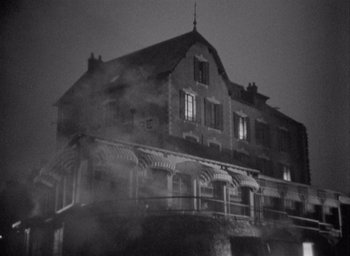 Movie still from “Monsieur Hulot's Holiday” (1953), directed by Jacques Tati – A black and white photo of a building with smoke coming out of the windows; Extreme Wide shot, Low angle