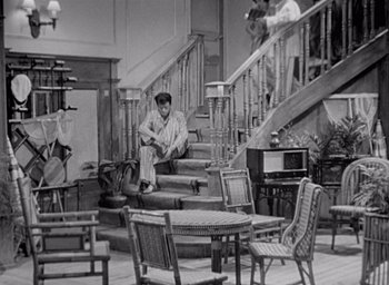 Movie still from “Monsieur Hulot's Holiday” (1953), directed by Jacques Tati – A man sitting on the stairs of a house; Wide shot, High angle