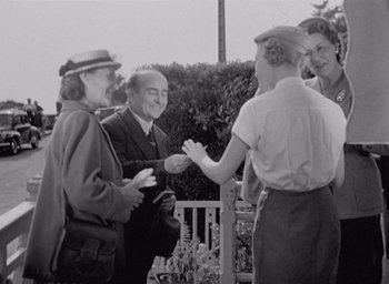 Movie still from “Monsieur Hulot's Holiday” (1953), directed by Jacques Tati – A black and white photo of a group of people talking; Medium shot, Over the shoulder angle