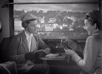 Movie still from “Monsieur Hulot's Holiday” (1953), directed by Jacques Tati – Two women are sitting at a table and one of the women is holding a book; Medium shot, High angle