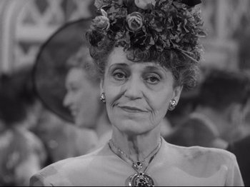 Movie still from “Monsieur Verdoux” (1947), directed by Charles Chaplin – An older woman wearing a hat with flowers on top of her head; Close Up shot, Over the shoulder angle