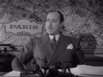 Movie still from “Monsieur Verdoux” (1947), directed by Charles Chaplin – An old black and white photo of a man sitting at a table in front of a map; Medium shot, High angle