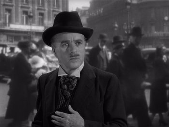 Movie still from “Monsieur Verdoux” (1947), directed by Charles Chaplin – A man in a suit and hat standing in front of a group of people; Close Up shot, Low angle