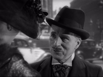 Movie still from “Monsieur Verdoux” (1947), directed by Charles Chaplin – An older man wearing a suit and a hat looking at a dog; Close Up shot, Over the shoulder angle