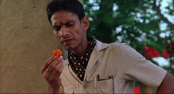 Movie still from “Monsoon Wedding” (2001), directed by Mira Nair – A man holding a piece of food in one hand and a knife in the other hand; Close Up shot, High angle