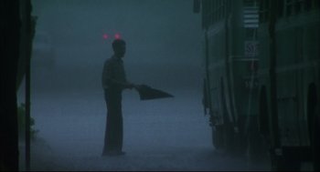 Movie still from “Monsoon Wedding” (2001), directed by Mira Nair – A man holding an umbrella standing next to a garbage truck; Wide shot, Low angle