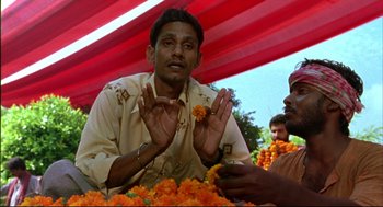 Movie still from “Monsoon Wedding” (2001), directed by Mira Nair – A man sitting in front of a pile of orange flowers; Medium shot, Low angle