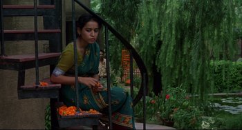 Movie still from “Monsoon Wedding” (2001), directed by Mira Nair – A woman sitting on a stair railing with a bunch of oranges; Medium shot, Low angle