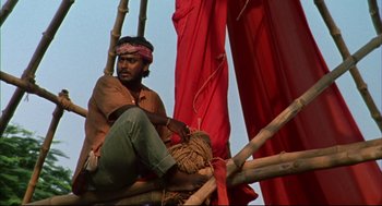 Movie still from “Monsoon Wedding” (2001), directed by Mira Nair – A man sitting on top of a pile of sticks; Medium shot, Low angle