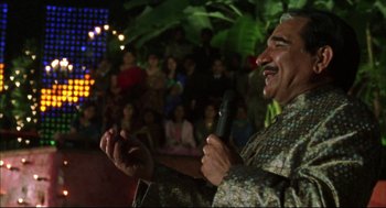 Movie still from “Monsoon Wedding” (2001), directed by Mira Nair – An older man holding a microphone in front of a crowd; Medium shot, Over the shoulder angle