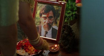 Movie still from “Monsoon Wedding” (2001), directed by Mira Nair – A picture of a man with a beard and glasses is in front of a candle; Extreme Close Up shot, High angle