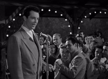 Movie still from “Moonrise” (1948), directed by Frank Borzage – A black - and - white photo of a man in a suit with a microphone; Medium shot, Low angle