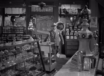 Movie still from “Moonrise” (1948), directed by Frank Borzage – A man standing in front of an old fashioned soda fountain; Wide shot, High angle