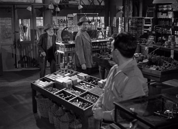 Movie still from “Moonrise” (1948), directed by Frank Borzage – A man and a woman looking at a table full of items; Wide shot, Over the shoulder angle
