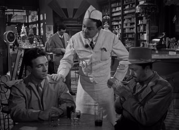 Movie still from “Moonrise” (1948), directed by Frank Borzage – A man standing at a table with two other men; Medium shot, Low angle
