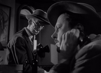 Movie still from “Moonrise” (1948), directed by Frank Borzage – A man in a suit and hat talking on a phone; Medium shot, Low angle