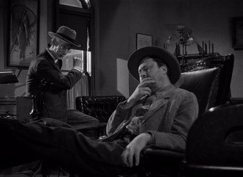 Movie still from “Moonrise” (1948), directed by Frank Borzage – A man sitting in a chair next to another man in a hat; Medium shot, Low angle