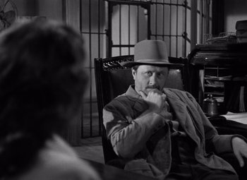 Movie still from “Moonrise” (1948), directed by Frank Borzage – A black and white photo of a man sitting in a chair; Medium shot, Over the shoulder angle