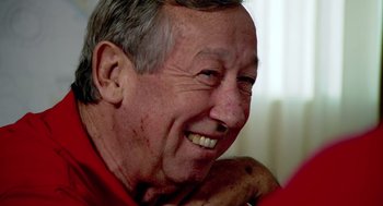 Movie still from “Morning Light” (2008), directed by Mark Monroe – An older man smiling and looking at the camera; Close Up shot, Over the shoulder angle