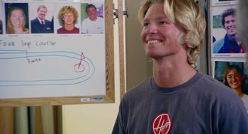 Movie still from “Morning Light” (2008), directed by Mark Monroe – A young man smiling in front of a picture of himself on the wall; Close Up shot, Over the shoulder angle