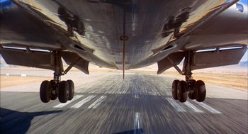 Movie still from “Morning Light” (2008), directed by Mark Monroe – View of the underside of an airplane on a runway; Wide shot, Low angle