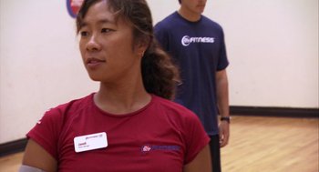 Movie still from “Morning Light” (2008), directed by Mark Monroe – A woman standing in front of a man in a gym; Close Up shot, Over the shoulder angle