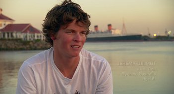 Movie still from “Morning Light” (2008), directed by Mark Monroe – A man sitting on the beach with a ship in the background; Close Up shot, Over the shoulder angle