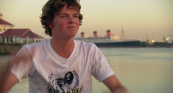 Movie still from “Morning Light” (2008), directed by Mark Monroe – A man in a white t - shirt is sitting on the beach; Close Up shot, Low angle