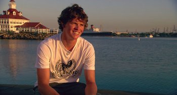 Movie still from “Morning Light” (2008), directed by Mark Monroe – A man sitting on a pier next to a body of water; Medium shot, Low angle