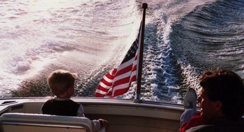 Movie still from “Morning Light” (2008), directed by Mark Monroe – A person on a boat in the water with an american flag on it; Wide shot, High angle