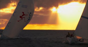 Movie still from “Morning Light” (2008), directed by Mark Monroe – The sun is setting over the ocean as a sailboat sails; Extreme Wide shot, Low angle