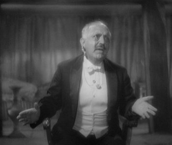 Movie still from “Morocco” (1930), directed by Josef von Sternberg – An old man in a suit sitting in a chair with his arms outstreched; Medium shot, Low angle