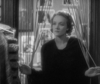 Movie still from “Morocco” (1930), directed by Josef von Sternberg – A black and white photo of a woman holding a bunch of sticks; Medium shot, Over the shoulder angle