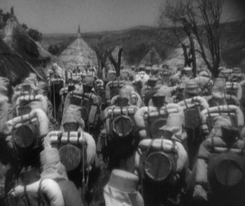 Movie still from “Morocco” (1930), directed by Josef von Sternberg – A black and white photo of a large group of people with backpacks; Wide shot, High angle