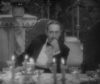 Movie still from “Morocco” (1930), directed by Josef von Sternberg – A black and white photo of a man sitting at a dinner table; Medium shot, High angle