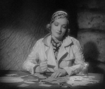 Movie still from “Morocco” (1930), directed by Josef von Sternberg – A woman sitting at a table with papers on it; Medium shot, High angle