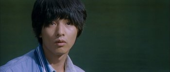 Movie still from “Mother” (2009), directed by Bong Joon Ho – A young man with black hair is looking at the camera; Close Up shot, Low angle