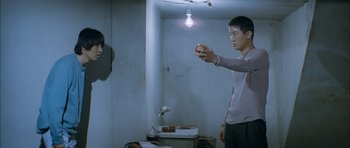Movie still from “Mother” (2009), directed by Bong Joon Ho – A man holding an object in his hand in a dimly - lit room; Medium shot, Over the shoulder angle