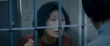 Movie still from “Mother” (2009), directed by Bong Joon Ho – A woman in a red sweater behind a metal fence; Close Up shot, High angle