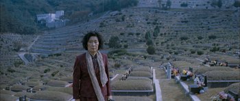 Movie still from “Mother” (2009), directed by Bong Joon Ho – A woman in a red suit standing in front of a cemetery; Wide shot, High angle