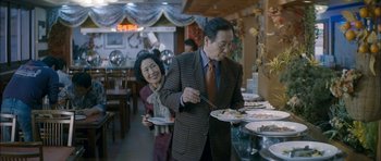 Movie still from “Mother” (2009), directed by Bong Joon Ho – A man and a woman are serving themselves at a buffet; Medium shot, Over the shoulder angle